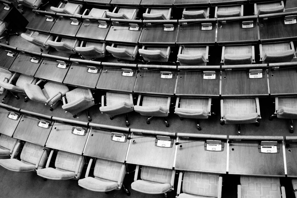Das Bild zeigt eine Reihe leere Stühle von oben in einem Plenum
